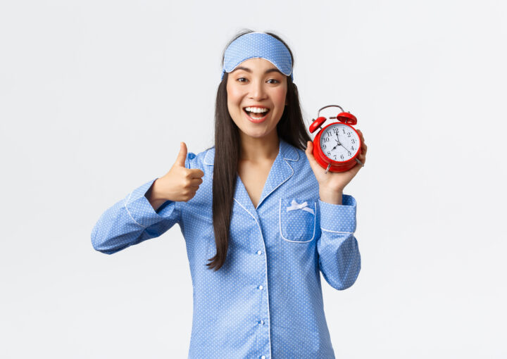 une photo d'une femme qui à un reveil dans la main avec un sourire et qui à un pouce vers le haut